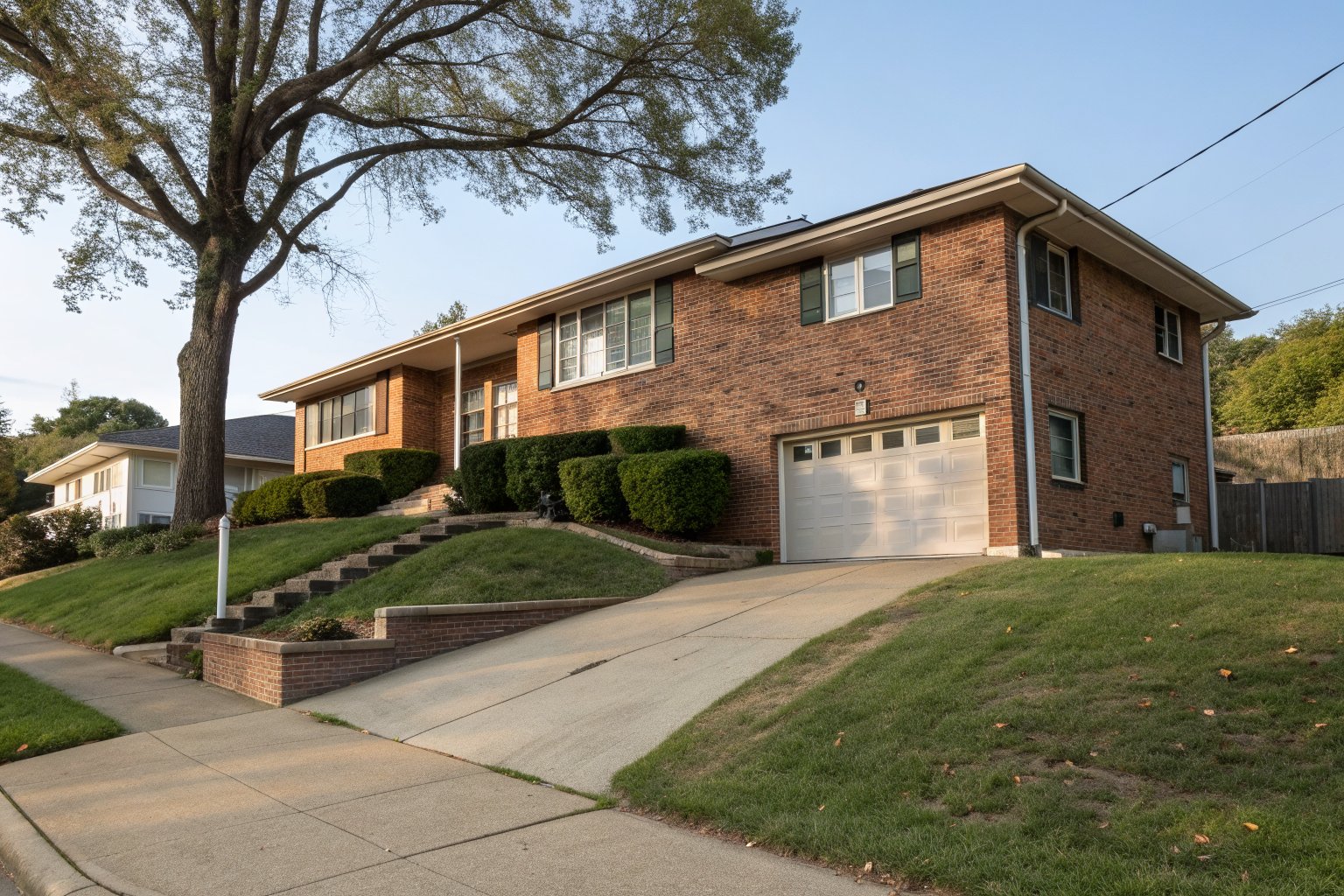 Split-level brick home with a lower garage and a sloped driveway behind a mature oak